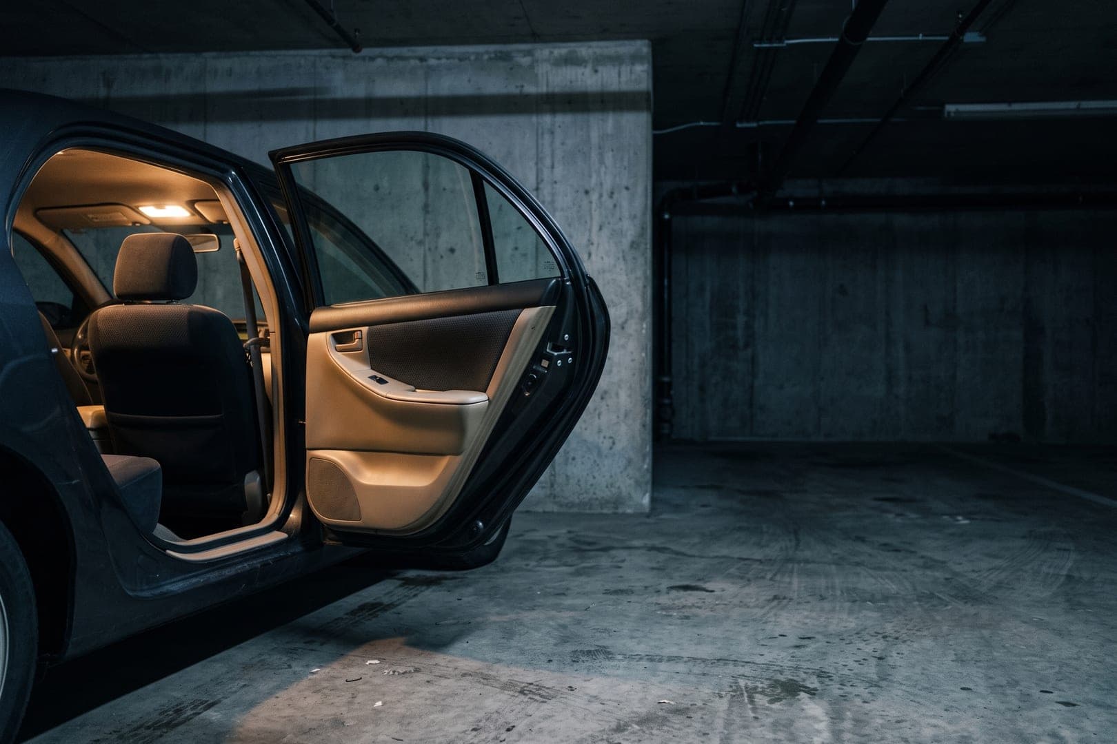 Puerta abierta de un coche oscuro de noche, con la luz interior encendida sobre el umbral y el asiento vacío al fondo.