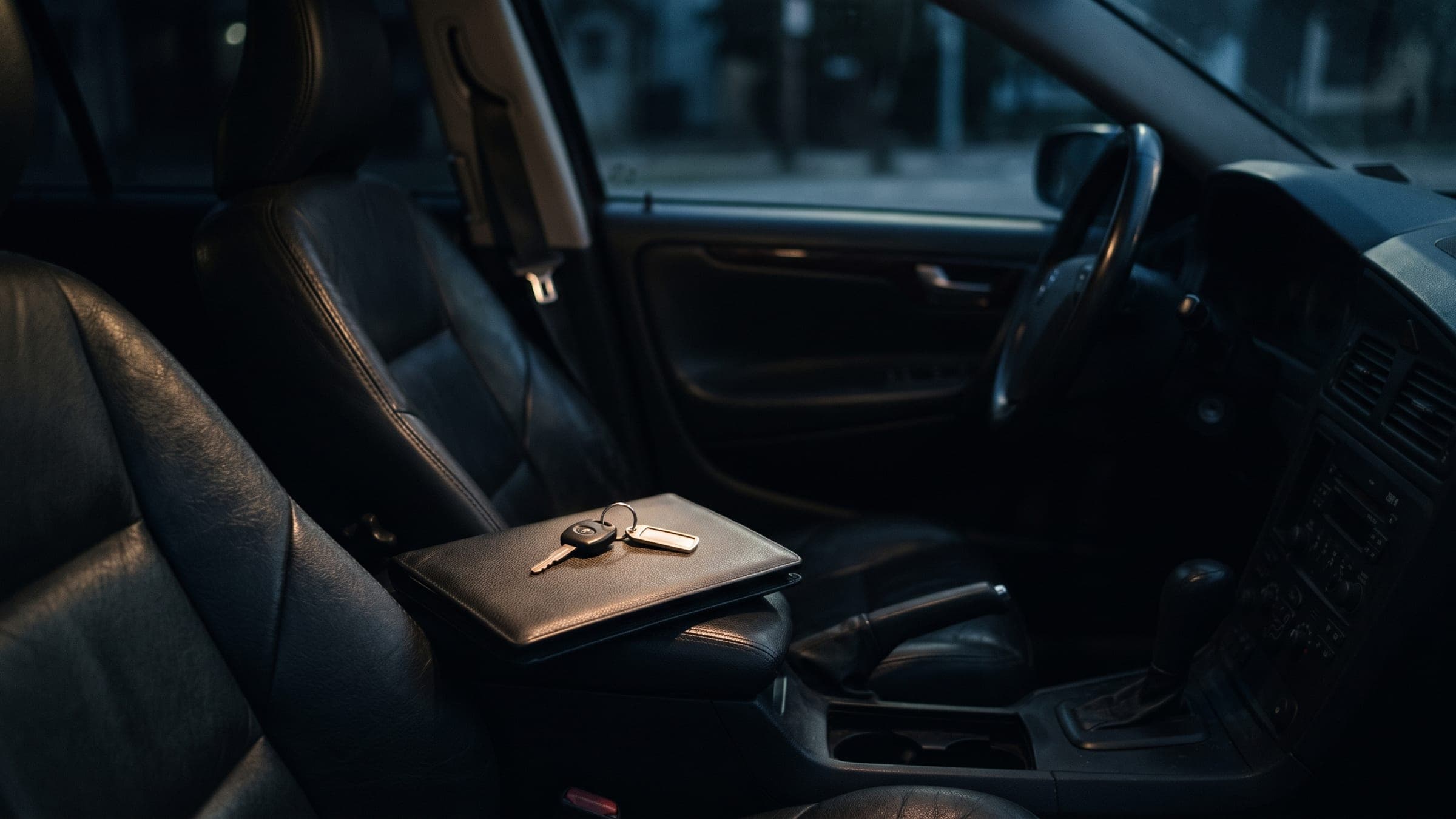Carpeta cerrada sobre el asiento de cuero de un coche de noche, con las llaves encima y una luz cálida cayendo desde el techo.